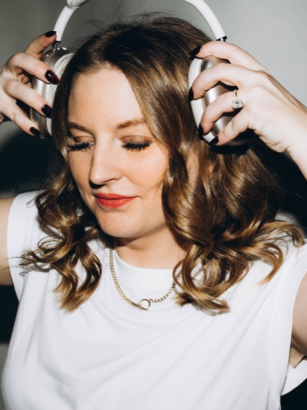 Emily Smale, eyes closed and smiling, holding a pair of headphones.